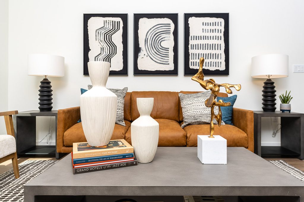 Stylish living room with a caramel leather sofa, black and white geometric rug, textured throw pillows, and abstract wall art.