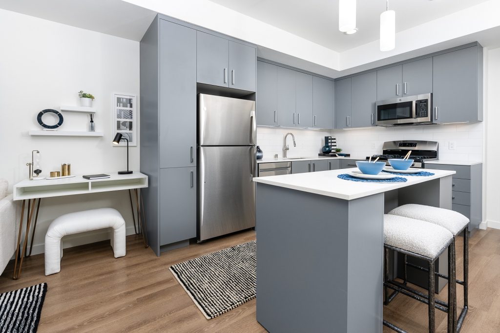 Modern kitchen with gray cabinetry, stainless steel appliances, and a central island with two padded stools under pendant lights.