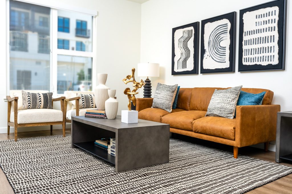 Elegant living room detail showing a leather sofa with patterned pillows, a large coffee table with books, and striking black and white art pieces on the wall.