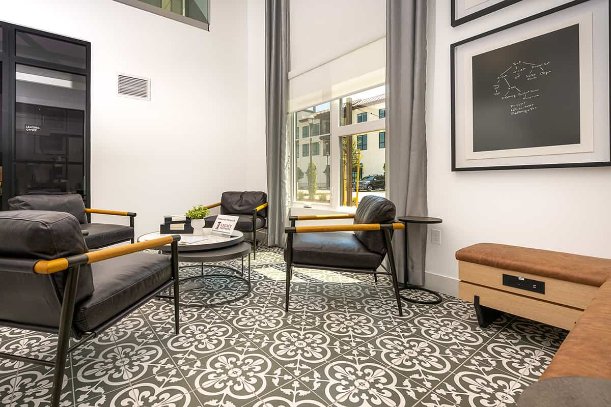 Crisp lobby with patterned floor, two charcoal armchairs, glass table with plant, framed art, and a window showing exterior buildings.
