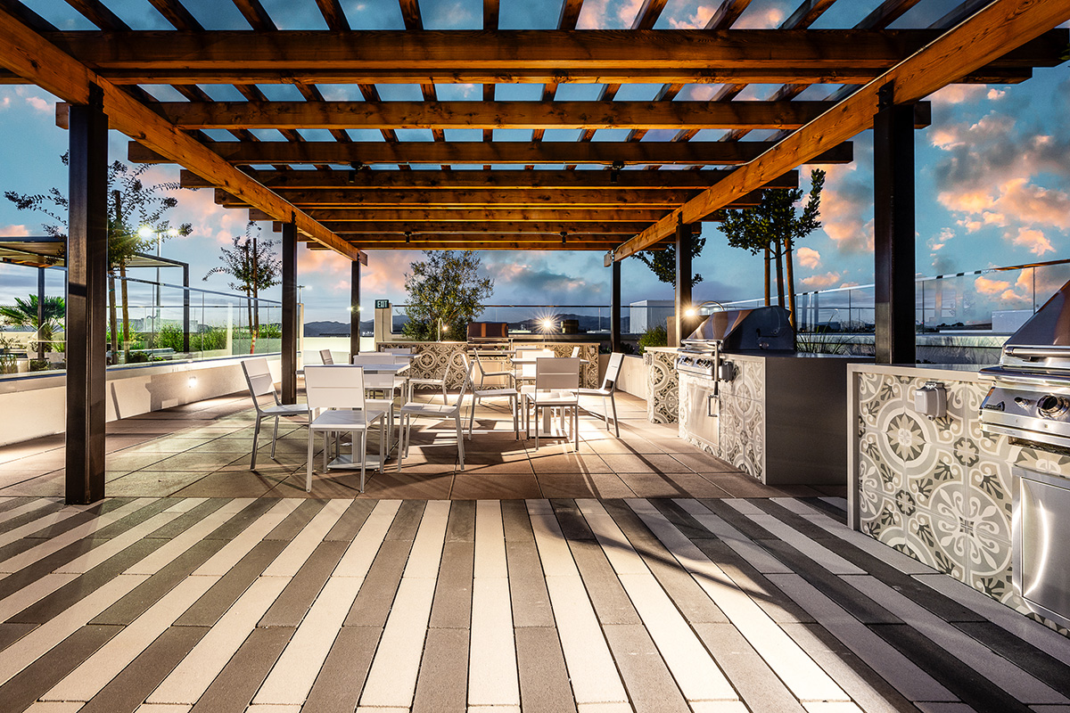 Outdoor rooftop terrace with wooden pergola, grill station, white dining set, and panoramic views.